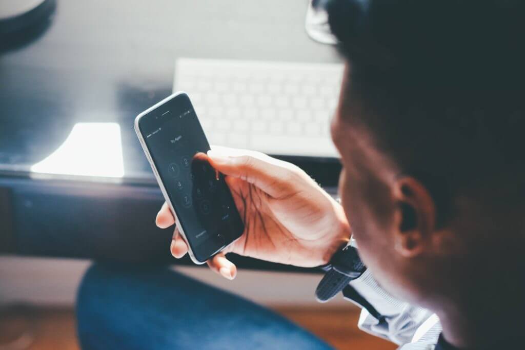 Un homme utilise son téléphone tout en étant assis à un bureau, concentré sur son appareil.